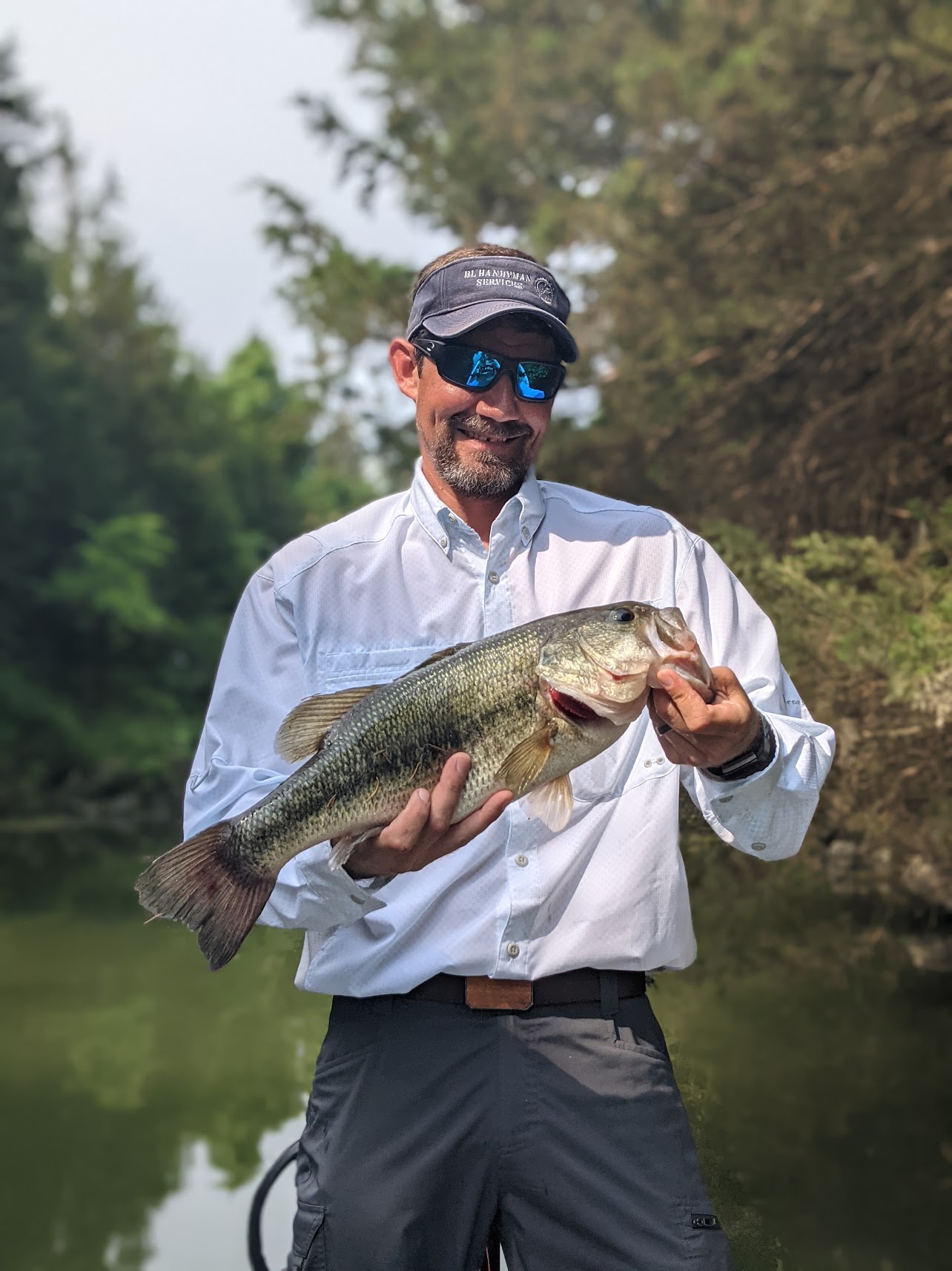 Adam Lazenby proudly displaying a large bass fish he caught, demonstrating his fishing skills and love for the outdoors