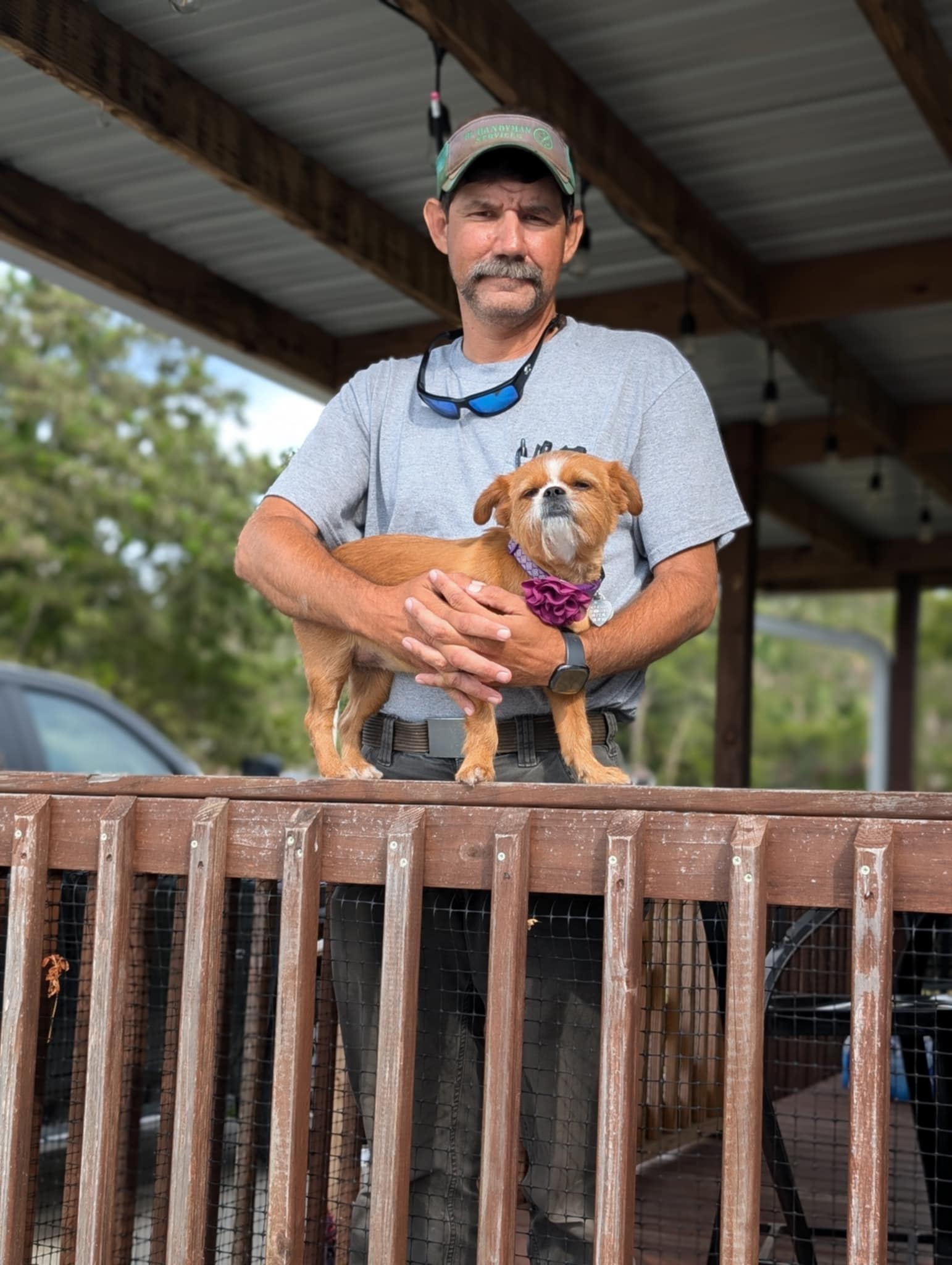 Adam Lazenby gently holding a small dog on a wooden deck, showcasing his compassionate nature with animals